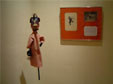 À direita, boneco da peça Onça e o Macaco (macaco), ao fundo moldura com desenho estudos sobre a peça.
<br/>
Local: Museu Alfredo Andersen - Rua Mateus Leme, 336 - Centro - Horário: 2ºa 6º feira: 9h00 às 18h00 - Sábados e Domingos das 10h00 às 16h00